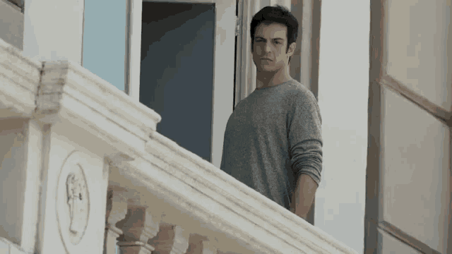 a man is standing on a balcony looking out a window .