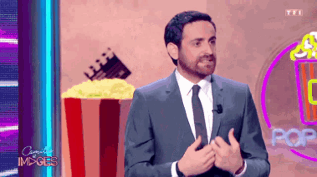 a man in a suit and tie stands in front of a popcorn bucket