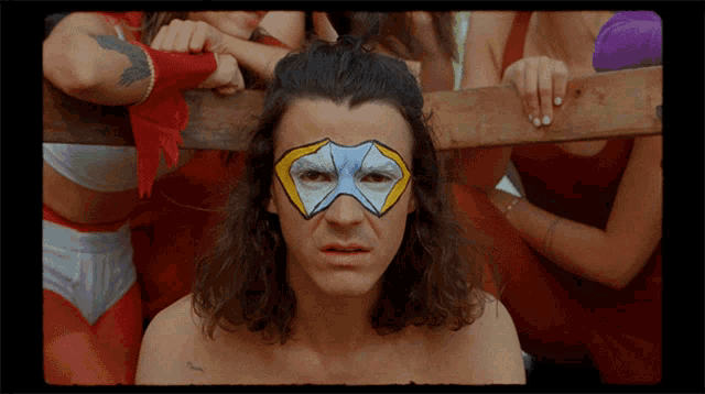 a man with a mask painted on his face stands in front of a group of women