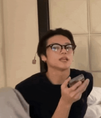 a man wearing glasses is holding a cell phone in his hand and making a funny face .