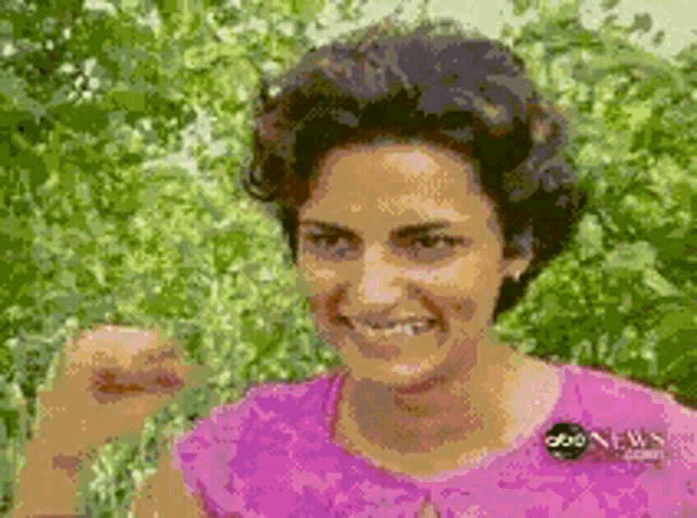 a woman in a pink shirt is smiling and making a fist