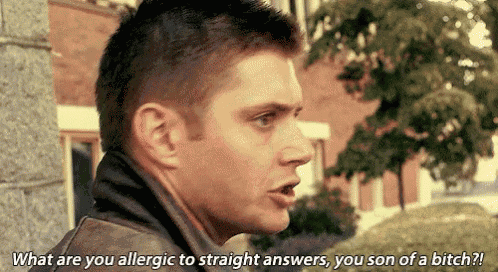 a man is talking to another man while standing in front of a building and trees .