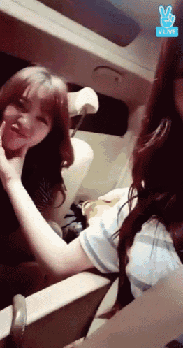 two girls are sitting in the back seat of a car with the vlive logo on the bottom right