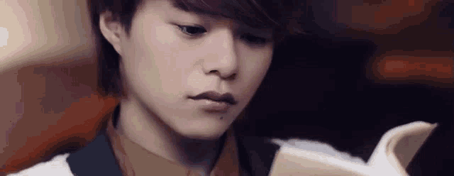 a young man is reading a book with a sad look on his face .