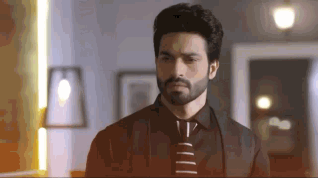 a man with a beard is wearing a black shirt and tie and standing in a room .