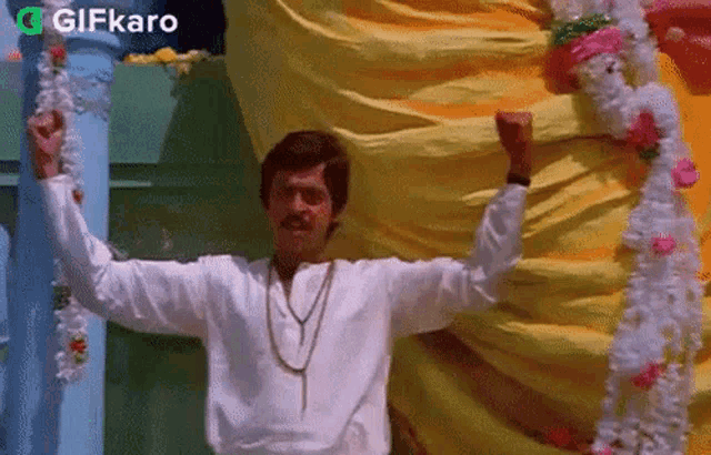 a man in a white shirt is standing in front of a yellow curtain with his arms outstretched .