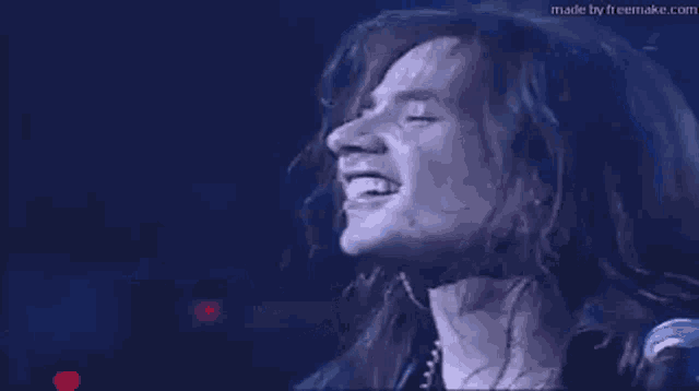 a man with long hair is standing in front of a microphone and singing into it .