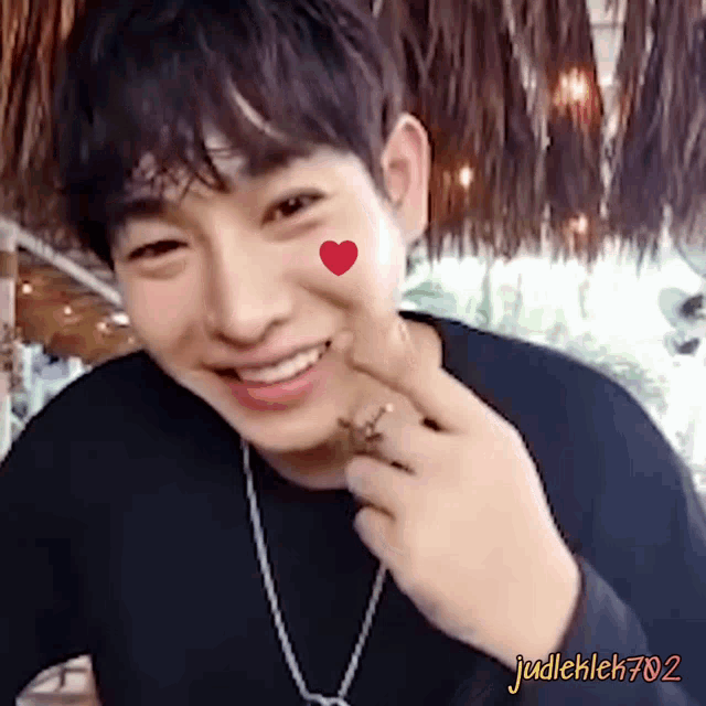 a young man with a red heart on his cheek is smiling and wearing a necklace
