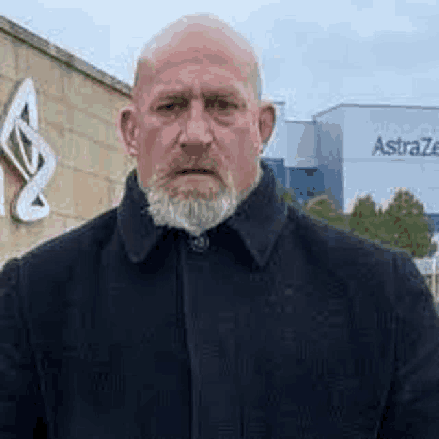 a bald man with a beard is standing in front of a building with a sign on it .