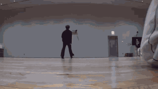 a man is standing on a wooden floor in a room while another man sits on the floor .