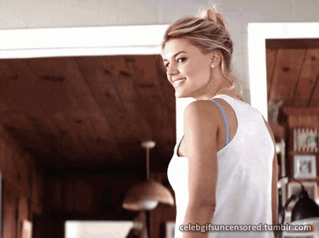 a woman in a white tank top is standing in a room with celebgifsuncensored.tumblr.com in the corner