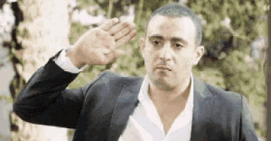 a man in a suit and white shirt is saluting with his hand in the air .