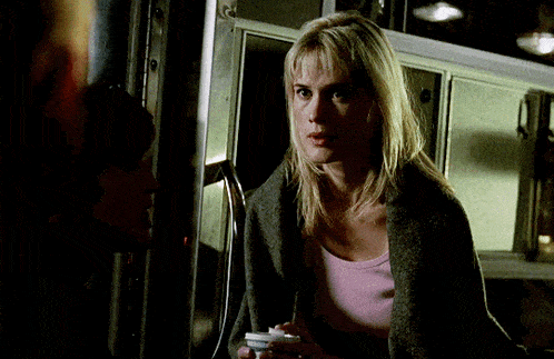 a woman in a pink shirt and a grey sweater is holding a cell phone