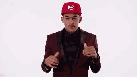 a man wearing a red hat and a maroon suit is giving two thumbs up .