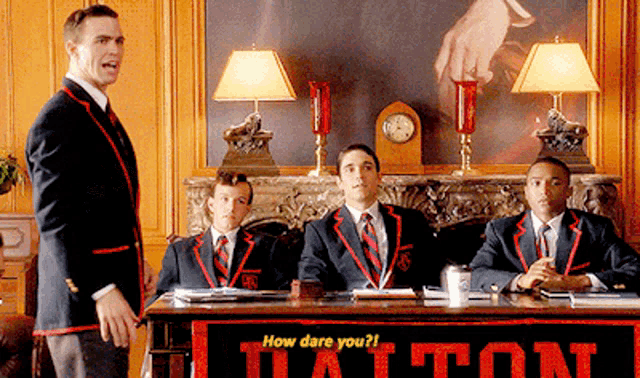 a group of men are sitting at a table with a banner that says how dare you