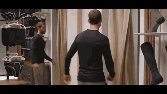 a man is standing in a dressing room in front of a mirror .