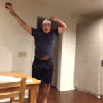 a man in a blue shirt and black shorts is standing in a room with his arms in the air