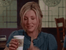 a woman is sitting at a table in a restaurant holding a cup of coffee and smiling .