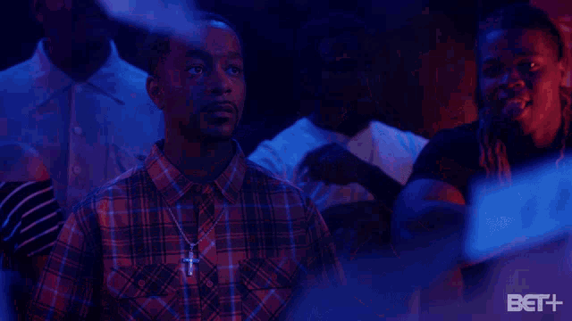 a man in a plaid shirt with a cross necklace is surrounded by smoke and a bet logo