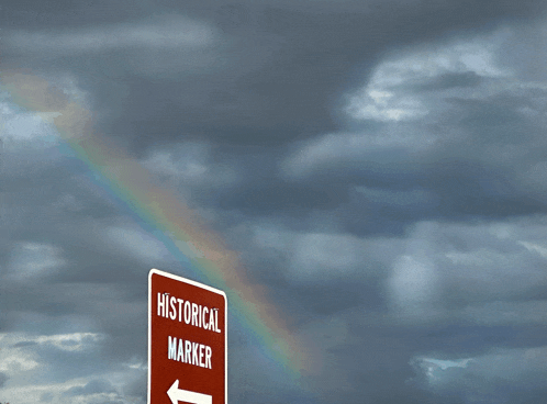 a historical marker sign with a rainbow in the sky