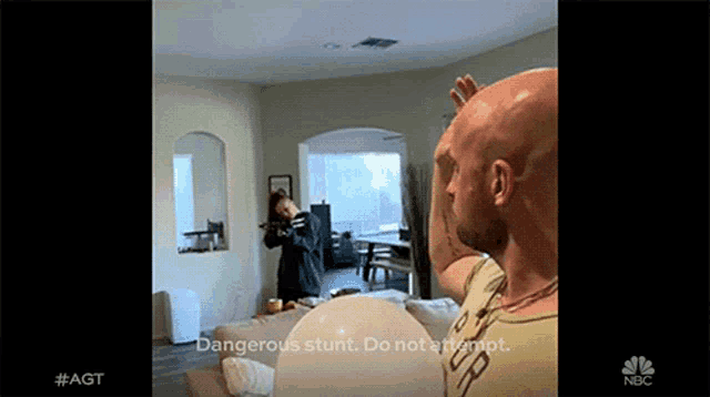 a bald man is standing in a living room with the words dangerous stunt do not attempt on the bottom of the screen