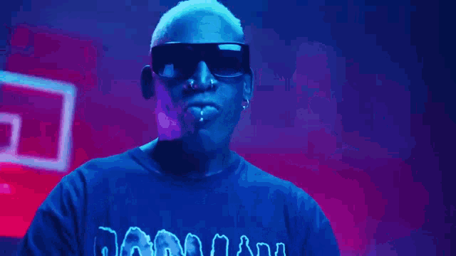 a man wearing sunglasses and a blue shirt is making a peace sign with his hands .