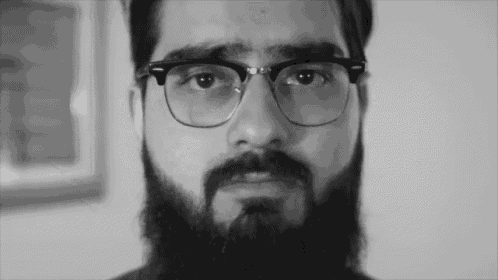 a man with glasses and a beard looks at the camera in a black and white photo