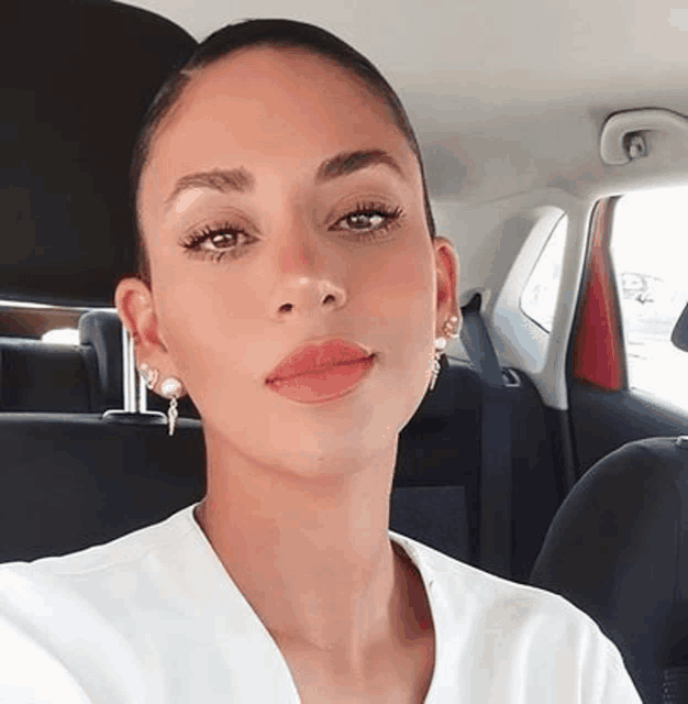 a woman is sitting in the back seat of a car wearing earrings and a white shirt .