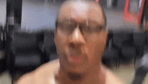 a man without a shirt is wearing glasses and making a funny face in a blurry photo .