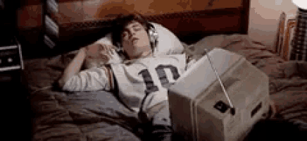 a young man is laying on a bed with headphones on and a television .