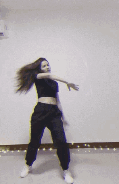 a woman wearing a black top and black pants is dancing