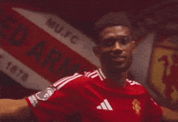 a man in a red manchester united jersey stands in front of a sign