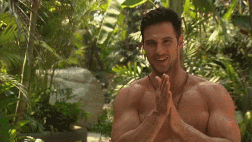 a shirtless man is clapping his hands and smiling in the jungle .