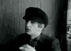 a man wearing a hat is smoking a cigarette in a black and white photo .