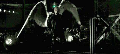 a man with angel wings is standing in a dark room with his wings spread .