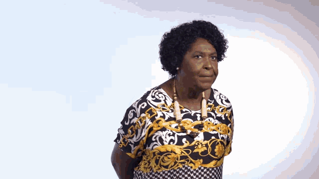 a woman with curly hair wearing a black and gold shirt and a necklace