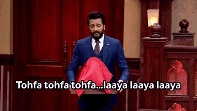 a man in a suit and tie is holding a red cloth in front of a sign that says tohfa tohfa