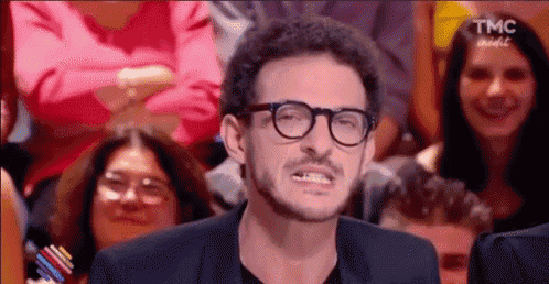 a man wearing glasses and a suit is making a funny face in front of a crowd of people .