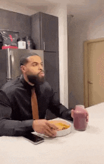 a man in a suit and tie is sitting at a table with a bowl of food and a cup of coffee .