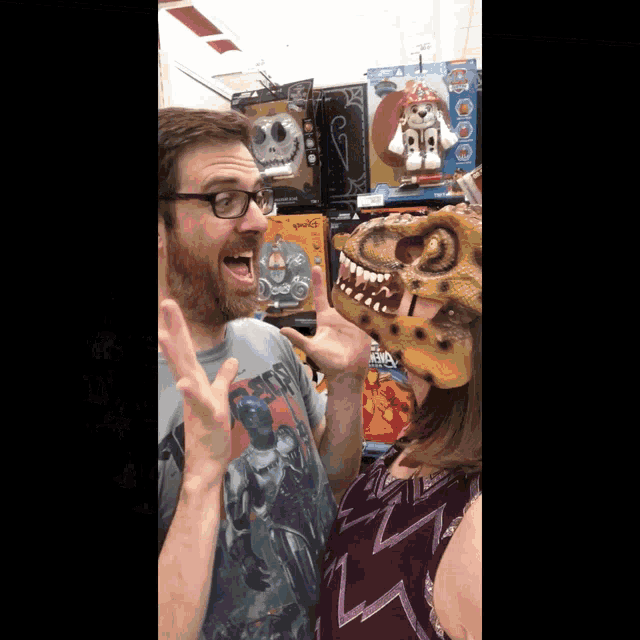 a man wearing a t-rex mask stands next to a woman wearing a pirate shirt