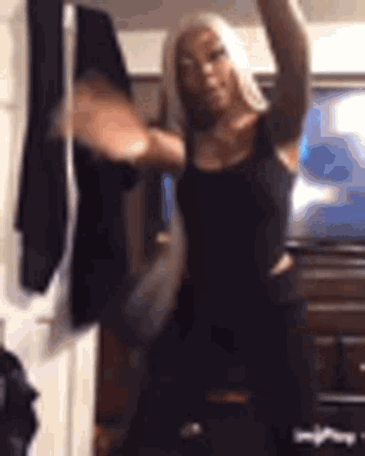 a woman in a black tank top is dancing in front of a television .