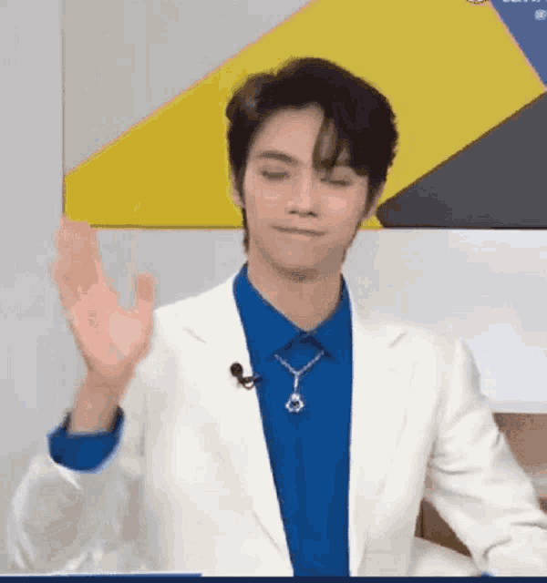 a man wearing a white jacket and a blue shirt is waving his hand in front of a microphone .
