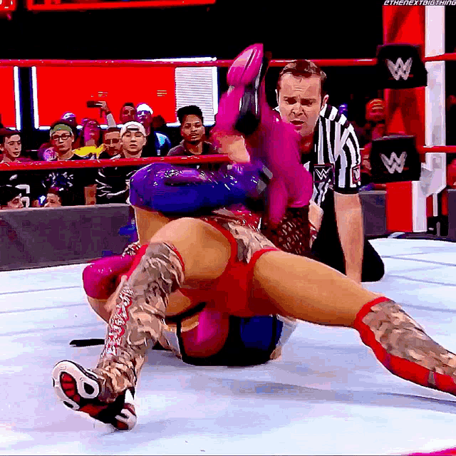 a woman in a wrestling ring with a referee and a w logo on the wall