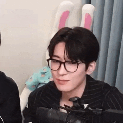a young man wearing glasses and bunny ears is sitting in front of a microphone in a room .