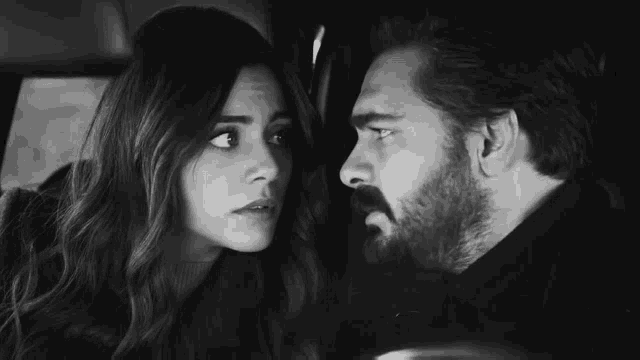 a black and white photo of a man and a woman looking at each other in a car .