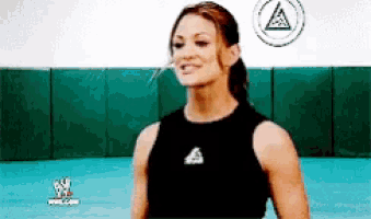 a woman in a black tank top is smiling in front of a wrestling mat