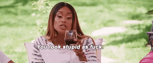 a woman is holding a glass of wine and saying `` you look stupid as fuck . ''