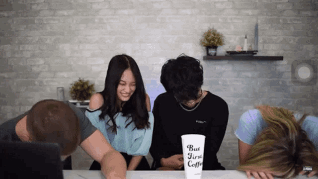 a group of people are sitting around a table with a cup that says but first coffee on it