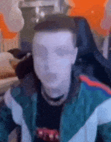 a blurry picture of a man wearing a green jacket and a black shirt sitting in a chair .