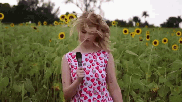 a woman in a strawberry dress is standing in a field of sunflowers holding a microphone